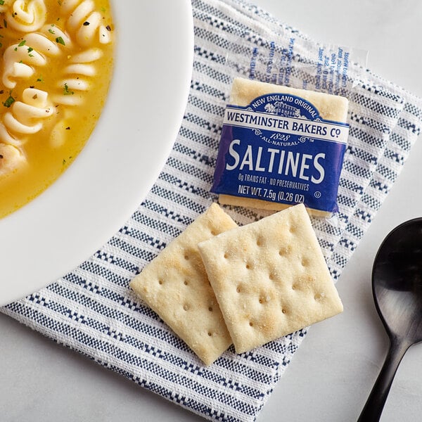 A bowl of soup with Westminster Saltine Crackers on a napkin.