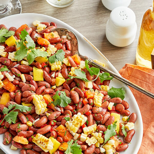 A plate of Goya red kidney beans and corn salad on a table with a stack of white plates.