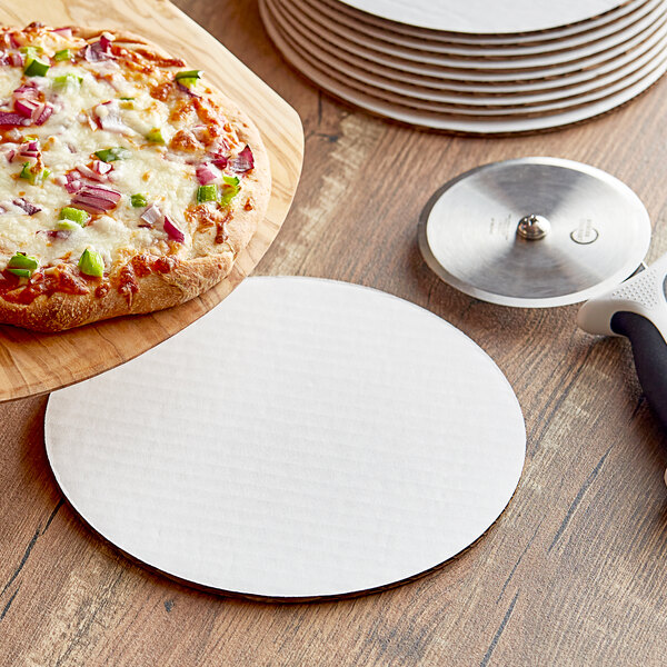 An 8" white corrugated pizza circle on a wooden surface next to a pizza cutter.