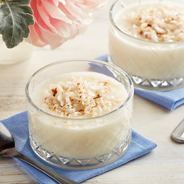 Two glasses of Goya cream of coconut with a spoon and coconut flakes.