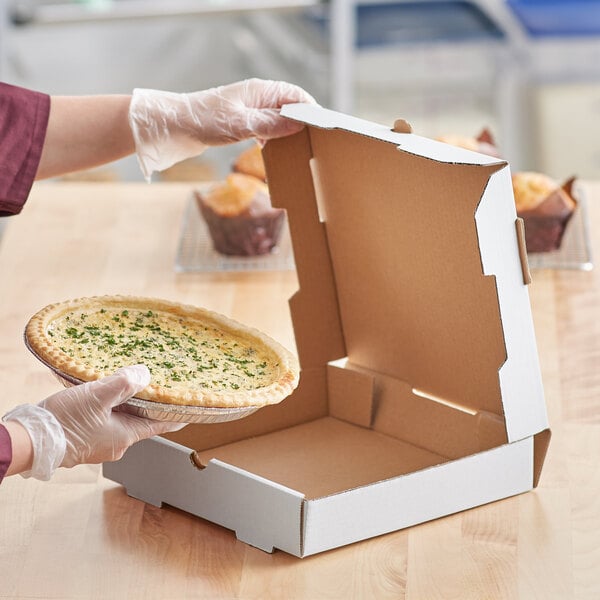 A person in gloves holding a pie in a white Choice bakery box.