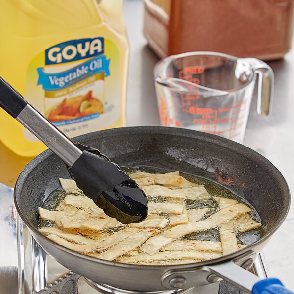 A frying pan with food in it on a stove with a bottle of Goya Pure Vegetable Oil.