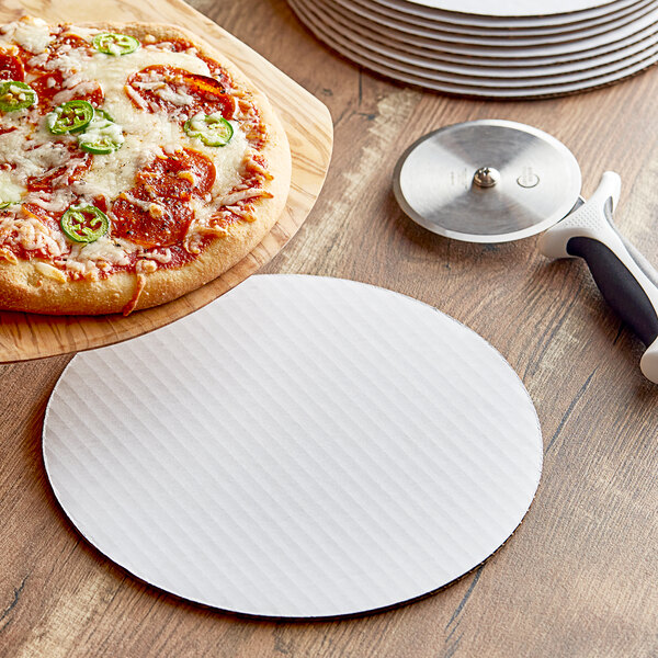 A pizza on a white corrugated circle next to a pizza cutter.