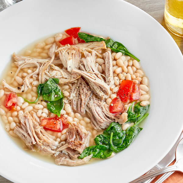 A bowl of white beans in soup with meat and vegetables.