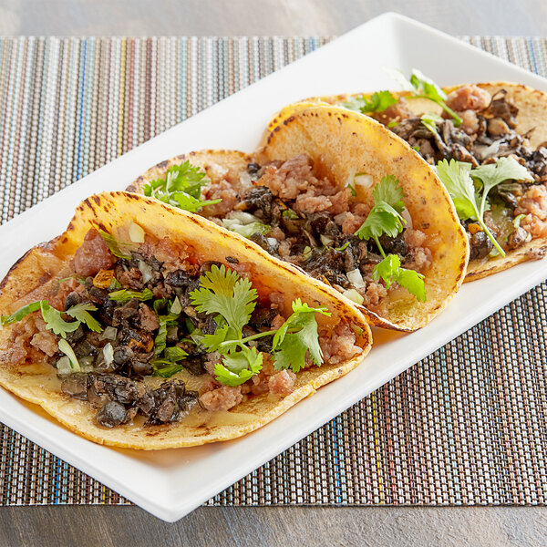 A plate of three tacos with garnish on a white table.