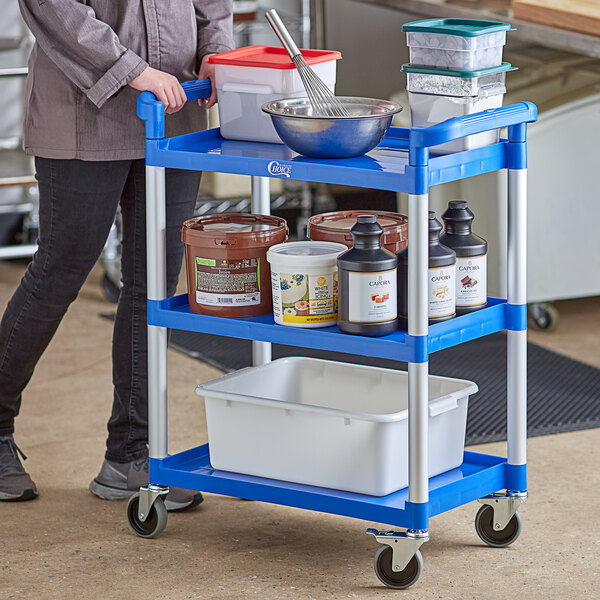A woman standing next to a blue Choice utility cart with white containers and a black pole.