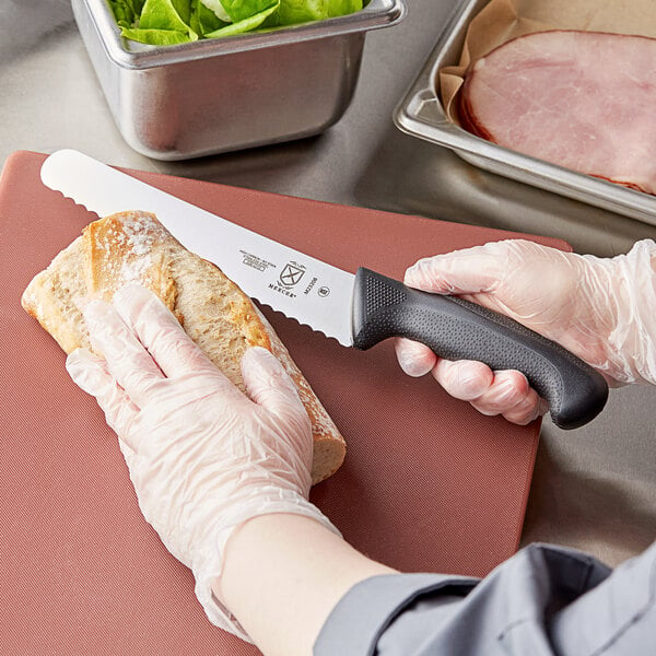A person using a Mercer Culinary Millennia bread knife to cut bread on a cutting board.