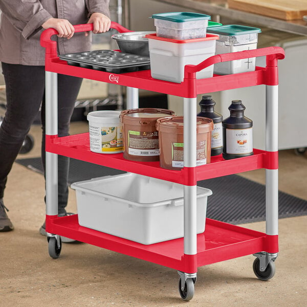 A woman using a red Choice utility cart with food containers.