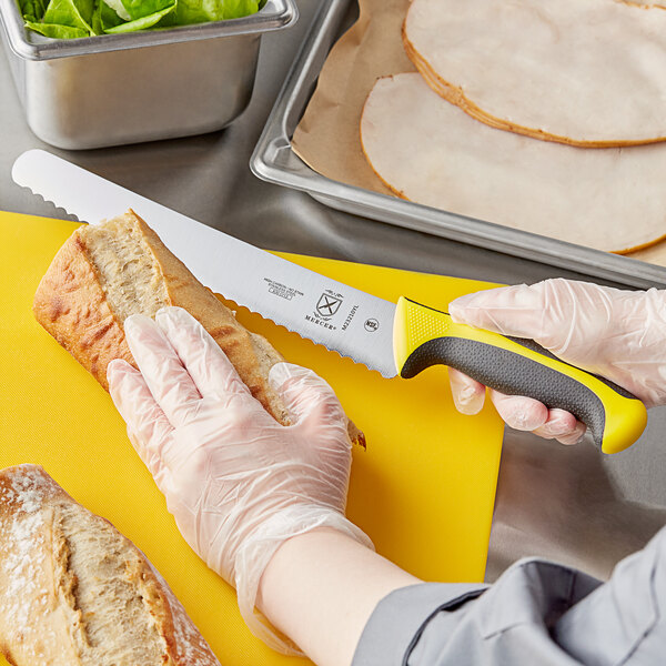 A person using a yellow Mercer Culinary Millennia bread knife to cut a sandwich.