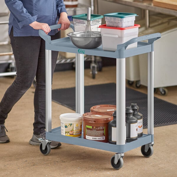 A woman pushing a gray Choice utility cart with containers on it.