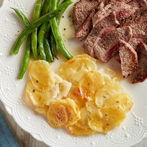 A plate of food with Idahoan Scalloped Potatoes, meat and vegetables on a table.