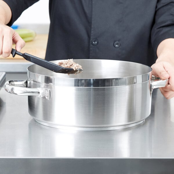 A chef using a Vollrath Centurion brazier pan to prepare food on a counter.