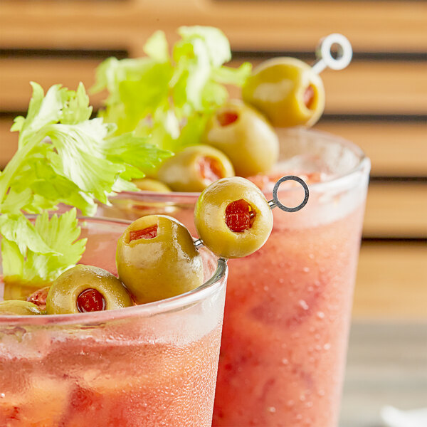 Two glasses of bloody marys with Goya Stuffed Manzanilla Olives and green peppers on a table.