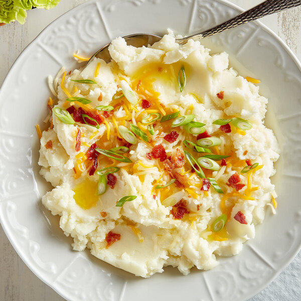 A plate of Idahoan mashed potatoes with bacon and cheese on a white background with a fork.