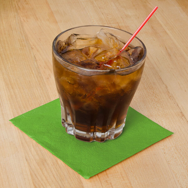 A Hoffmaster lime green beverage napkin under a glass with brown liquid and a straw.