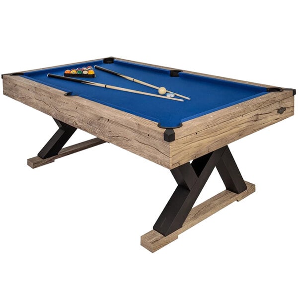An American Legend Kirkwood pool table with royal blue cloth and rustic blond wood legs, with cue sticks and balls on it.