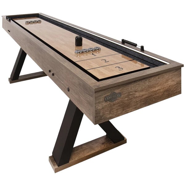 A wood and metal shuffleboard table with accessories on it.
