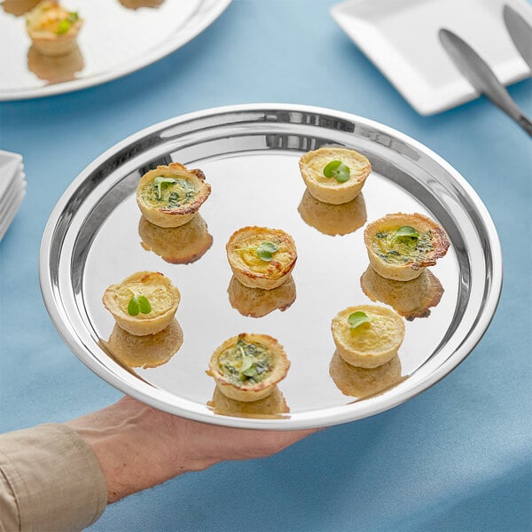 A hand holding an Acopa stainless steel catering tray with small appetizers on it.