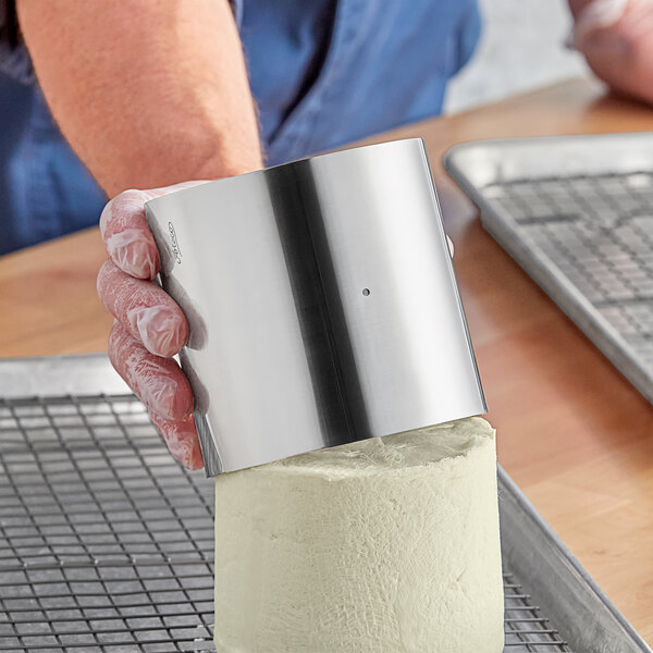 A hand holding a metal cylinder, the Ateco stainless steel round cheese mold.
