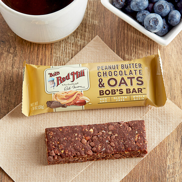 A Bob's Red Mill Peanut Butter Chocolate & Oats Bar on a napkin next to a bowl of blueberries.