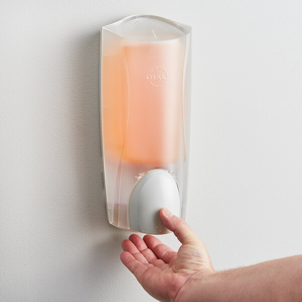 A hand pressing a Dial manual hand soap dispenser on a wall.