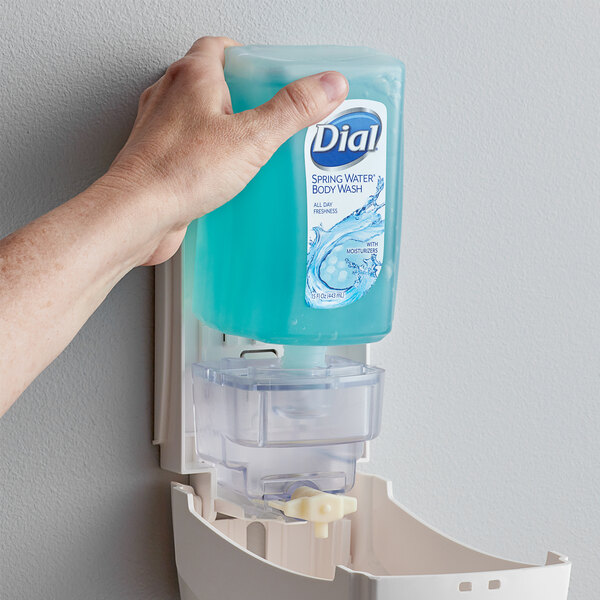 A person's hand pushing a bottle of blue Dial body wash