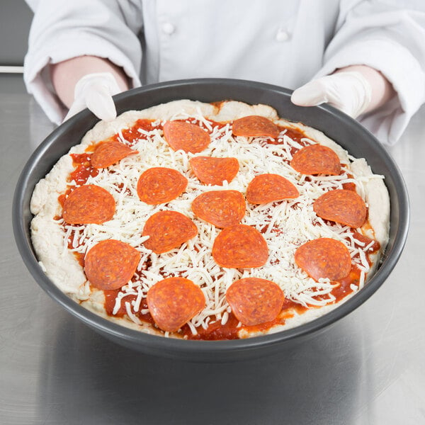 A person holding a Chicago Metallic deep dish pizza pan with a pizza topped with pepperoni and cheese.