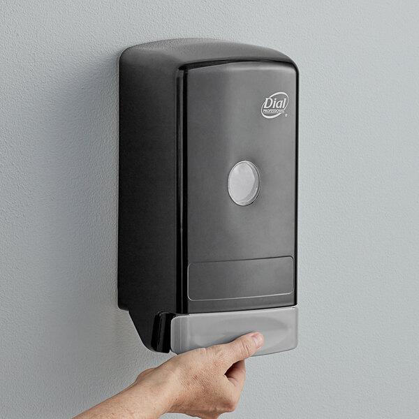 A hand using a Dial black manual liquid soap dispenser.