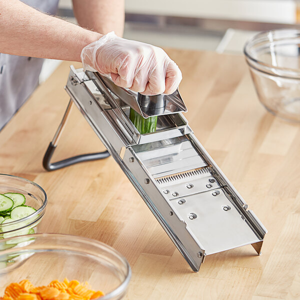 A person using a Choice stainless steel mandoline to slice cucumbers.
