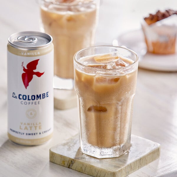A La Colombe Vanilla Latte in a glass on a table with a can of La Colombe Vanilla Latte.