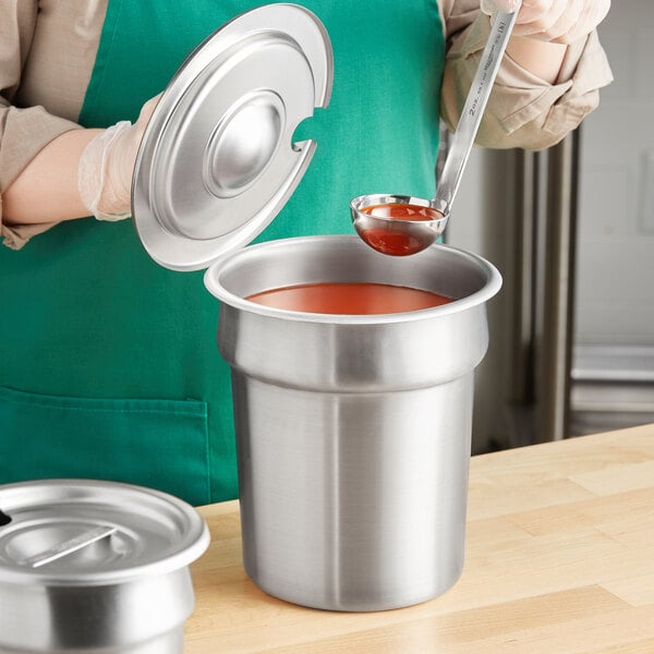 A woman using a Jacob's Pride ladle to pour red sauce into a Vollrath stainless steel inset.