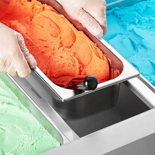 A person holding a stainless steel gelato pan filled with orange and blue ice cream.