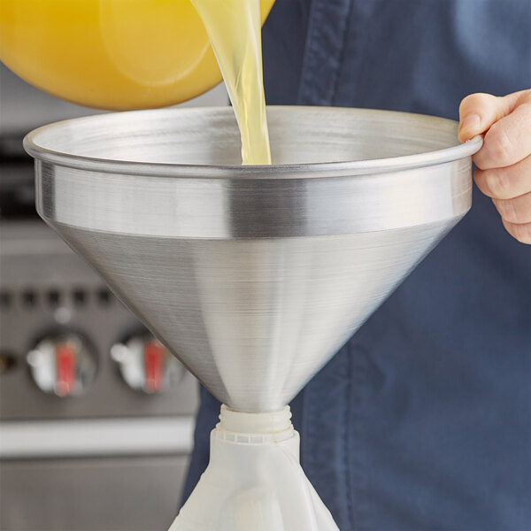 A person pouring orange juice into an American Metalcraft aluminum funnel.