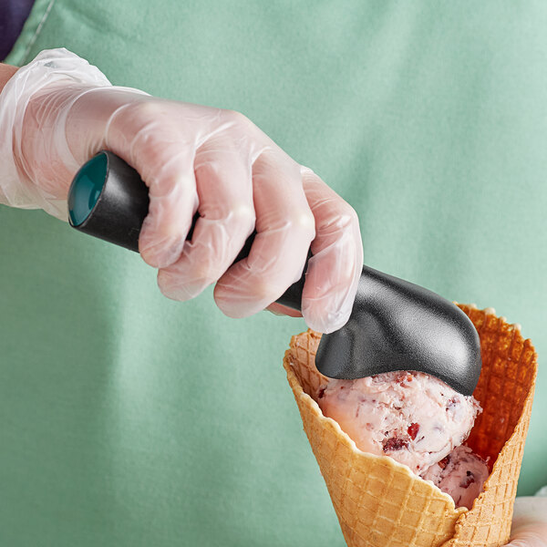 A person in gloves using a Choice #16 green non-stick ice cream scoop to scoop ice cream.