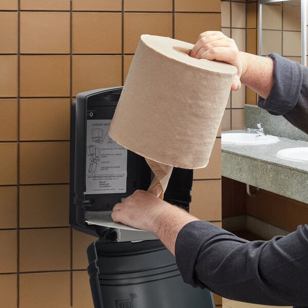 A man's hand holding a Lavex 2-Ply Natural Kraft paper towel roll.