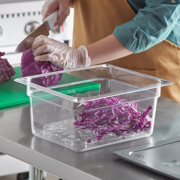 A person wearing gloves uses a knife to cut purple cabbage into a plastic container.