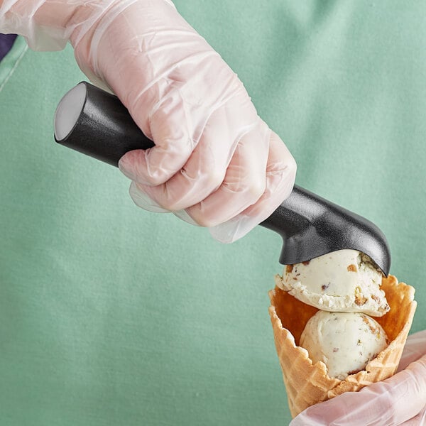 A person in gloves using a Choice #24 silver ice cream scoop to serve white ice cream.