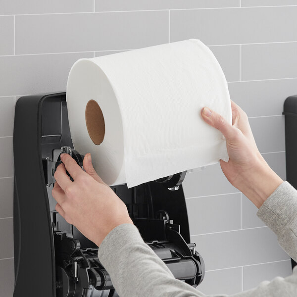 A person holding a Lavex Select white paper towel roll in a blank room.