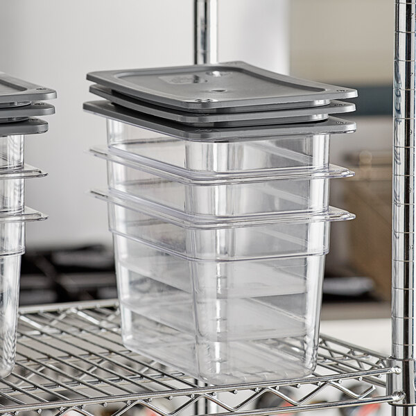 Three Vigor clear plastic food pans with secure sealing covers on a metal rack.