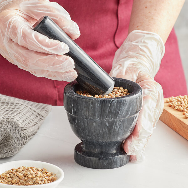 A person in gloves grinding seeds in a Fox Run marble mortar.