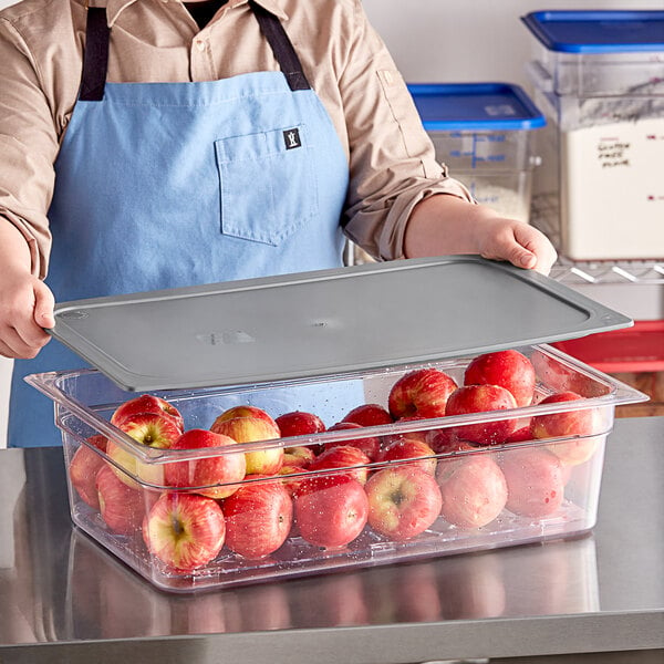 A person holding a clear Vigor food pan filled with red apples.