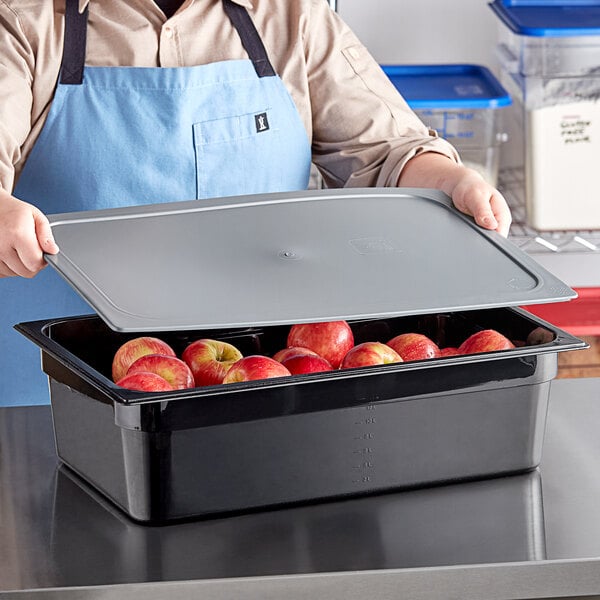A man in an apron holding a Vigor black food pan with apples on a tray.