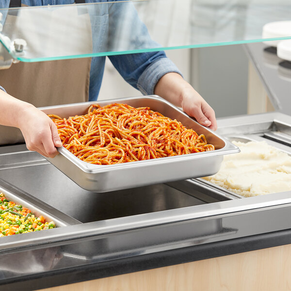 A person holding a Vigor 2/3 size stainless steel steam table pan full of spaghetti.