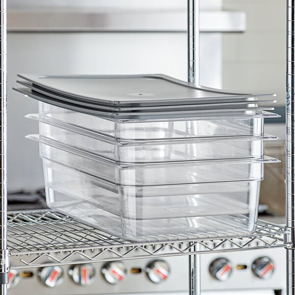 A stack of Vigor clear plastic food pans with secure sealing covers on a metal shelf.
