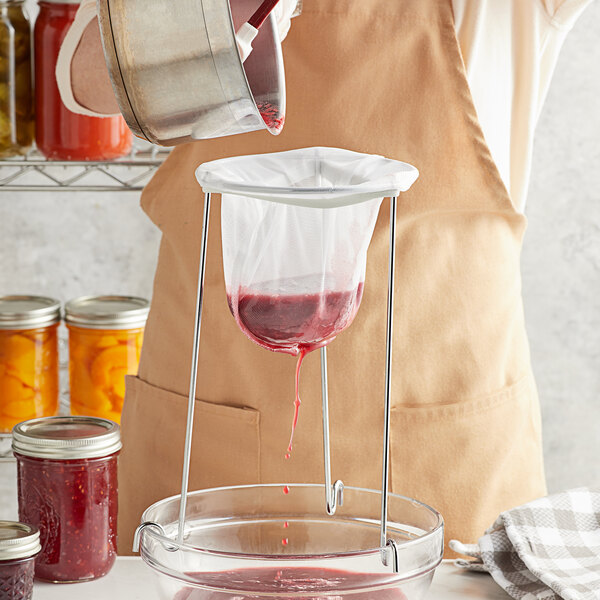 A person pouring red liquid into a jar using a Fox Run jelly and jam strainer bag.