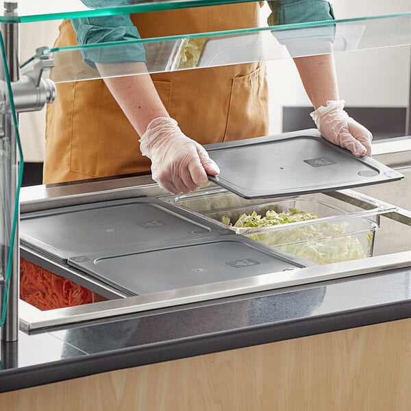 A person wearing gloves using a Vigor clear plastic food pan to fill a tray with food.