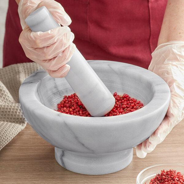 A person using a Fox Run white marble mortar to grind red pepper.