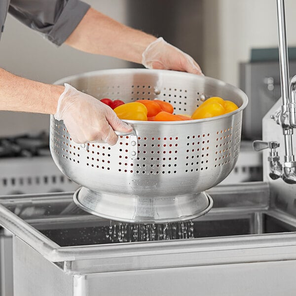 A person in gloves washing tomatoes in a Choice aluminum colander.