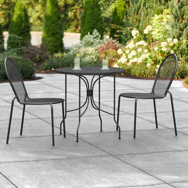 A Lancaster Table & Seating Harbor black outdoor table with two chairs on a patio.