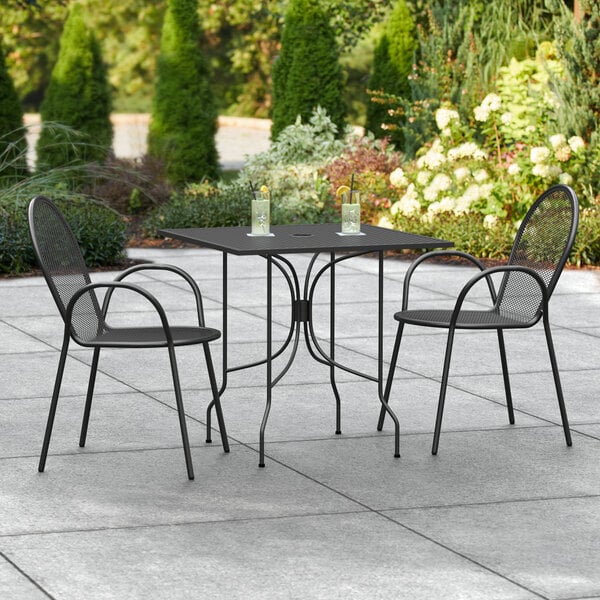 A Lancaster Table & Seating Harbor black table with two black chairs on a concrete patio.